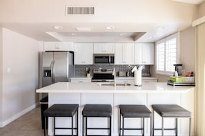 A modern kitchen with white cabinetry, stainless steel appliances, a central island with bar stools, and a window providing natural light. - Scottsdale Sahuaro Villa 🌵⛳ Private Pool Near Mayo Clinic & McDowell Mtns (Scottsdale)