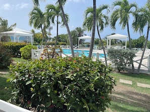 A pool area with palm trees, a white gazebo, and a covered seating area. - Relaxing Gated Condo w/ Huge Pool, Walk to Beach (Christiansted)