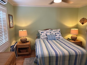 A bedroom with a bed, two bedside tables with lamps, a wall clock, and a framed picture. - Relaxing Gated Condo w/ Huge Pool, Walk to Beach (Christiansted)