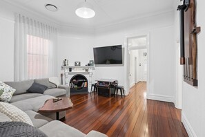 A living room with a fireplace, a television mounted on the wall, and a wooden floor.