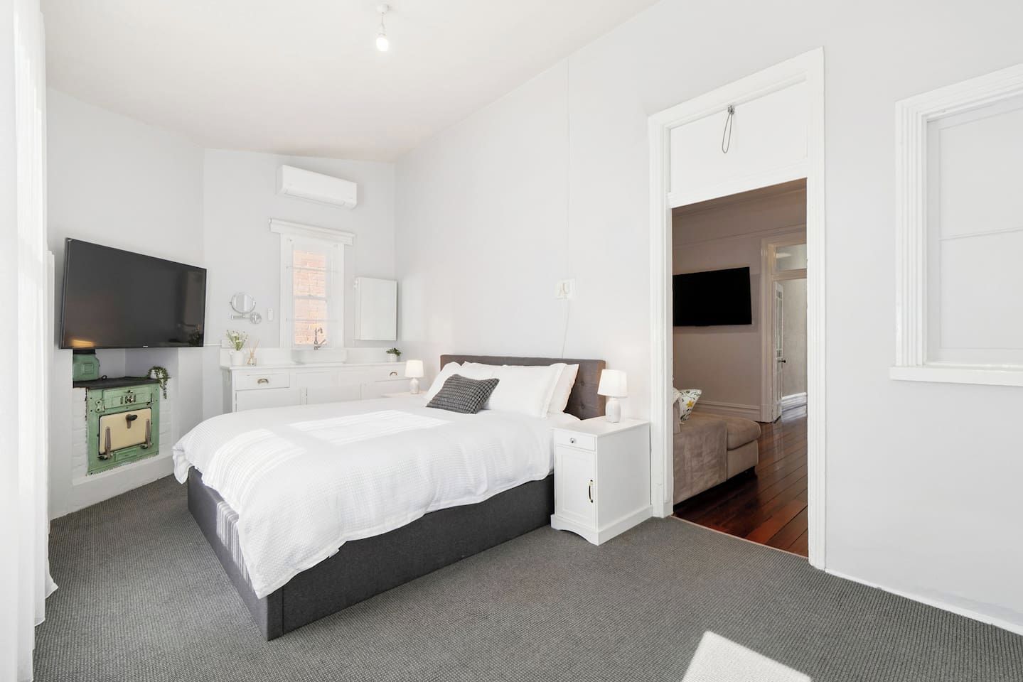 A modern bedroom with a large bed, bedside tables, a TV, and a green vintage-style stove.