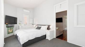 A modern bedroom with a large bed, bedside tables, a TV, and a green vintage-style stove.