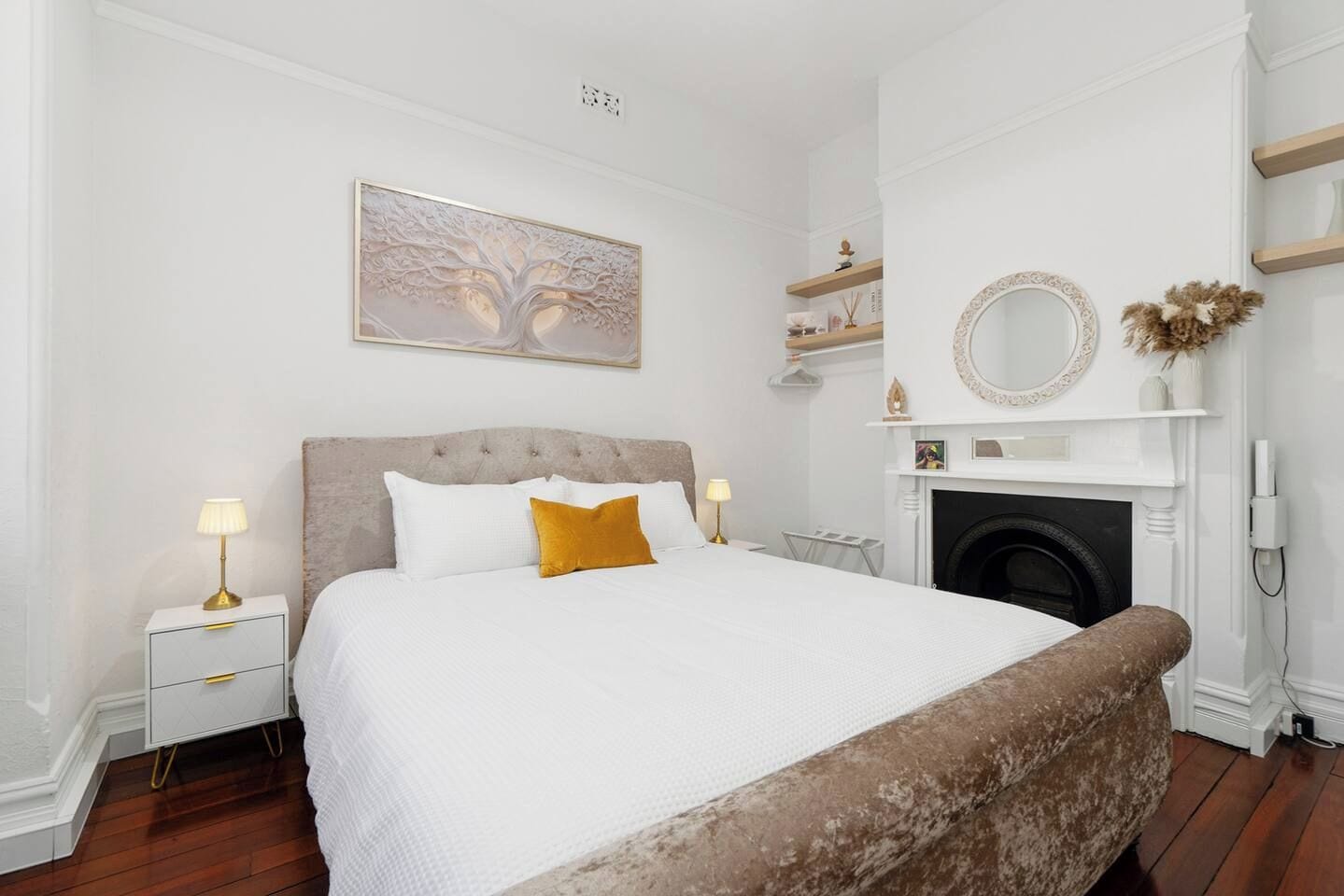 A bedroom with a bed, bedside tables, a fireplace, and a wall-mounted mirror.