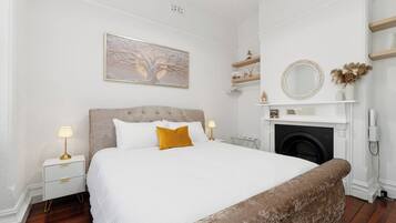 A bedroom with a bed, bedside tables, a fireplace, and a wall-mounted mirror.