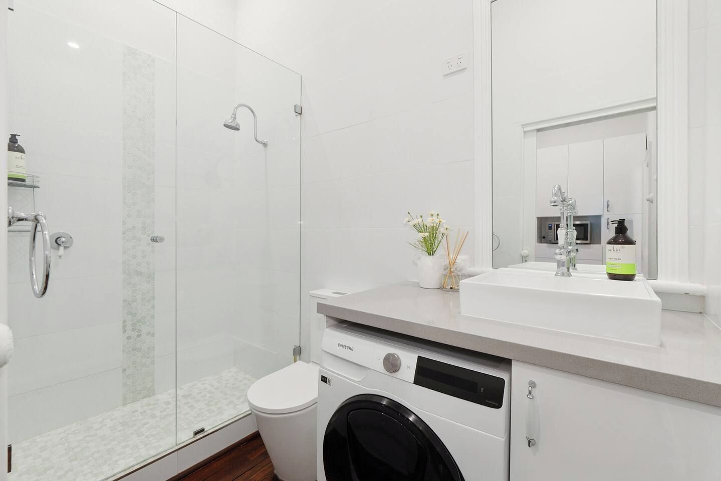 A modern bathroom with a glass-enclosed shower, a white sink, and a built-in washing machine.