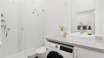 A modern bathroom with a glass-enclosed shower, a white sink, and a built-in washing machine.