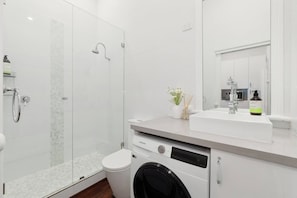 A modern bathroom with a glass-enclosed shower, a white sink, and a built-in washing machine. - Heart of Northbridge | Food, Bars & Culture (Northbridge)