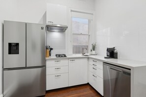 A compact kitchen with white cabinetry, a built-in dishwasher, a stove, and a coffee maker.