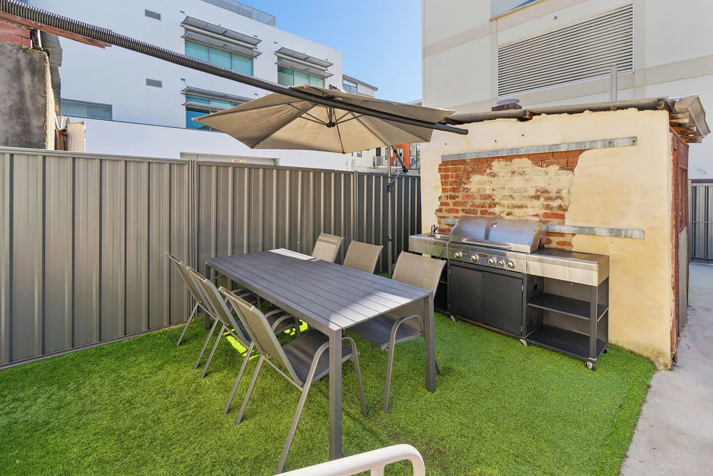 An outdoor patio with a table and chairs, a grill, and a covered area.