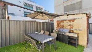 Un patio exterior con mesa y sillas, una parrilla y un espacio cubierto.