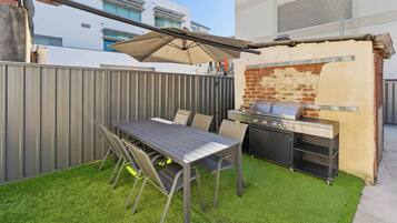 An outdoor patio with a table and chairs, a grill, and a covered area.