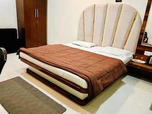 A bed with a brown bedspread, a white pillow, and a headboard with vertical lines. - HOTEL MANSAROVAR (Omkareshwar)