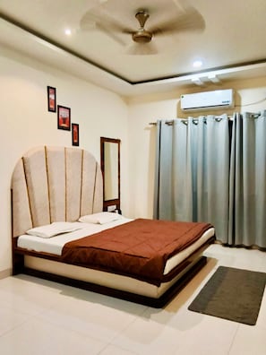 A bedroom with a bed, a ceiling fan, an air conditioning unit, and curtains. - HOTEL MANSAROVAR (Omkareshwar)
