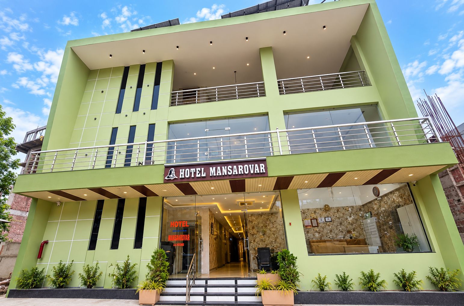 A two-story hotel with a green facade, a visible entrance, and a sign reading 'HOTEL MANSAROVAR.'