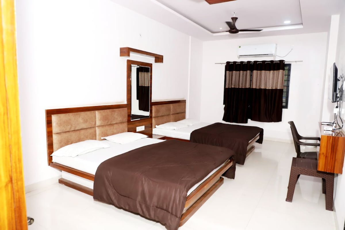 A hotel room with two beds, a desk, a chair, a ceiling fan, and an air conditioning unit.