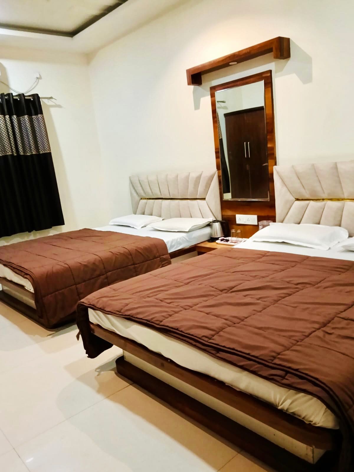 A hotel room with two beds, a large mirror, and a window with curtains.