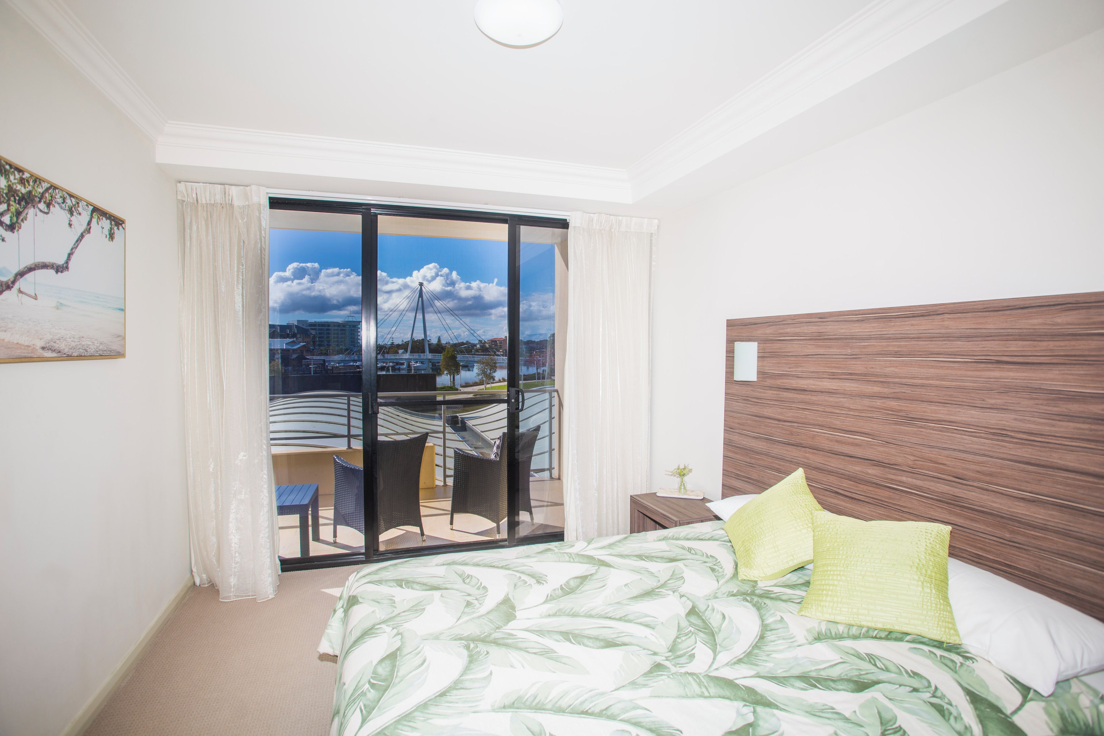 A hotel room with a bed, a view of a cityscape, and a balcony with chairs.