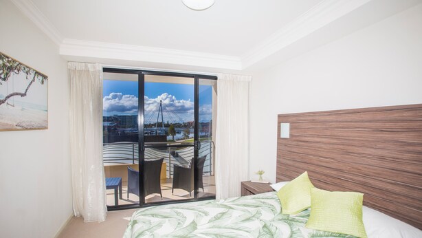 Quarto de hotel com cama, vista para a cidade e varanda com cadeiras.