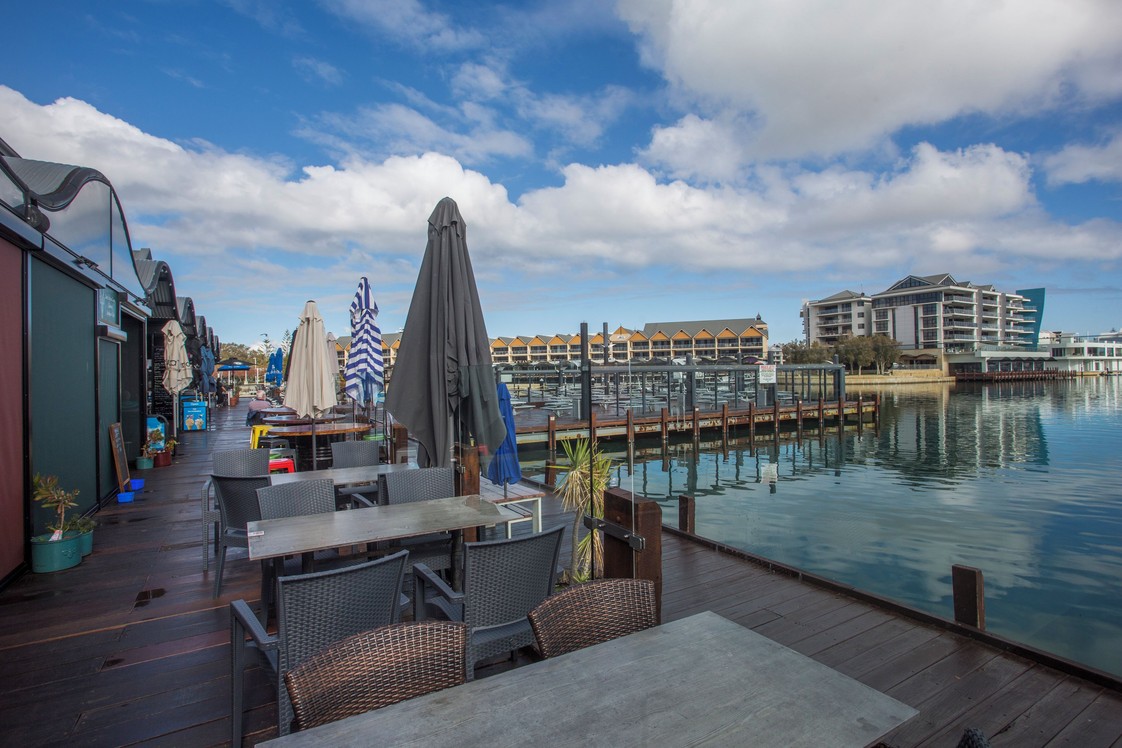 A waterfront patio with outdoor seating, a marina in the background, and a hotel building across the water.
