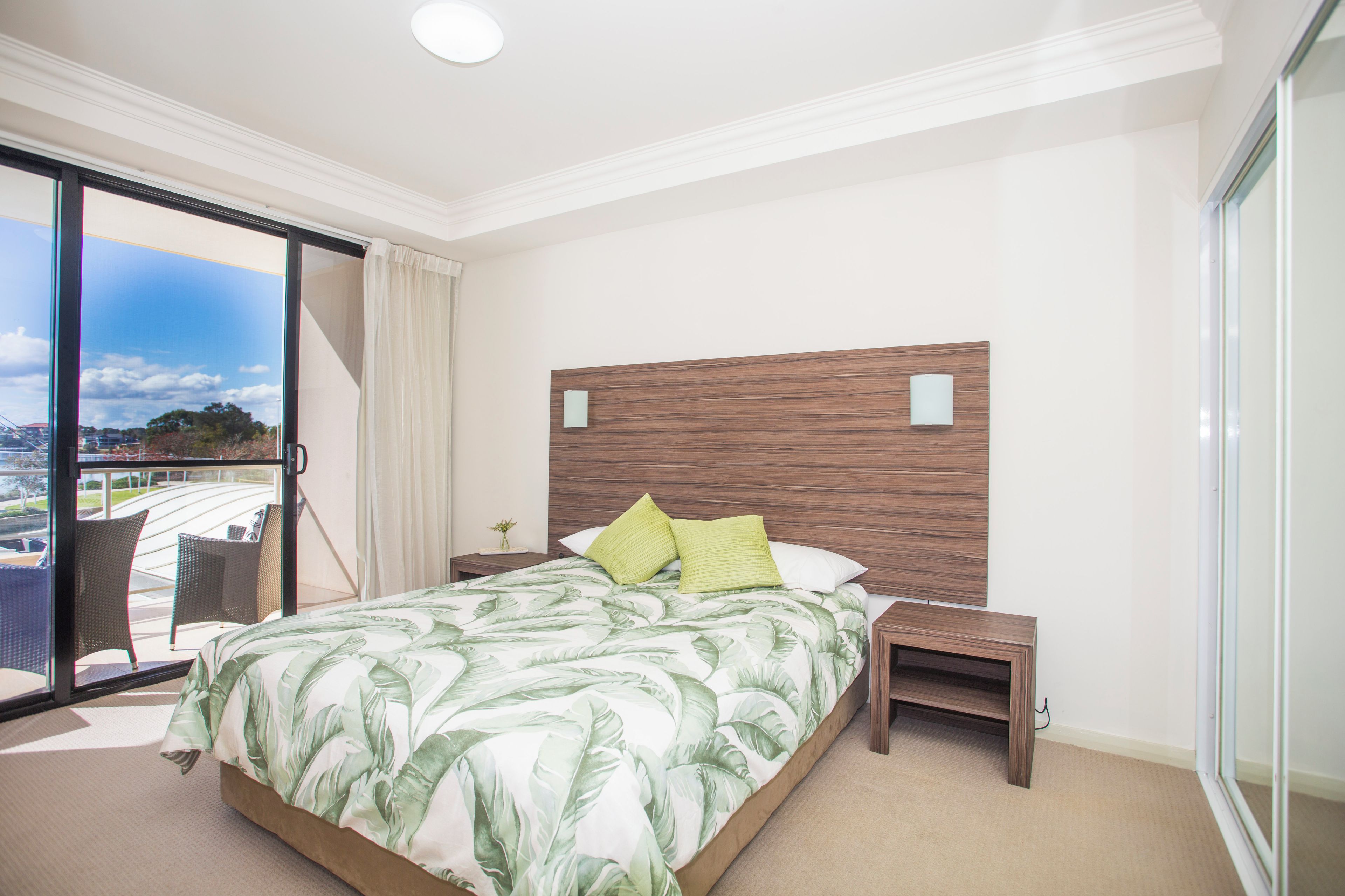A hotel room with a large bed, a nightstand, a chair, and a view of the outdoors.