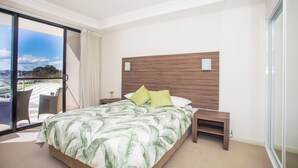 Quarto de hotel com uma cama grande, mesa de cabeceira, cadeira e vista para o exterior.