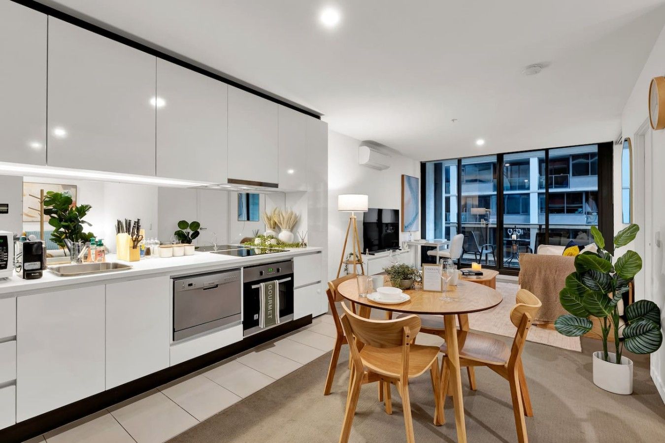 Een moderne keuken met inbouwapparatuur, een eetgedeelte met houten stoelen en een uitzicht op de stad door grote ramen.