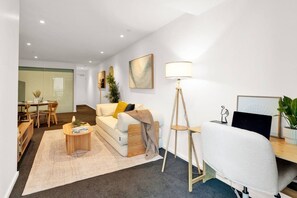 A modern living room with a sofa, coffee table, and a desk with a lamp. - L27 2BR 2Bath | Free Parking, Pool, Gym| Sth Cross (Melbourne)
