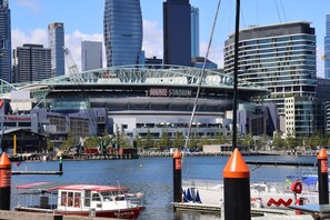 A waterfront view with a prominent stadium in the background, boats docked at the marina, and modern high-rise buildings. - L27 2BR 2Bath | Free Parking, Pool, Gym| Sth Cross (Melbourne)
