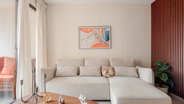 Uma sala de estar moderna com um sofá seccional, uma mesa de centro com objetos decorativos e um grande quadro abstrato na parede.