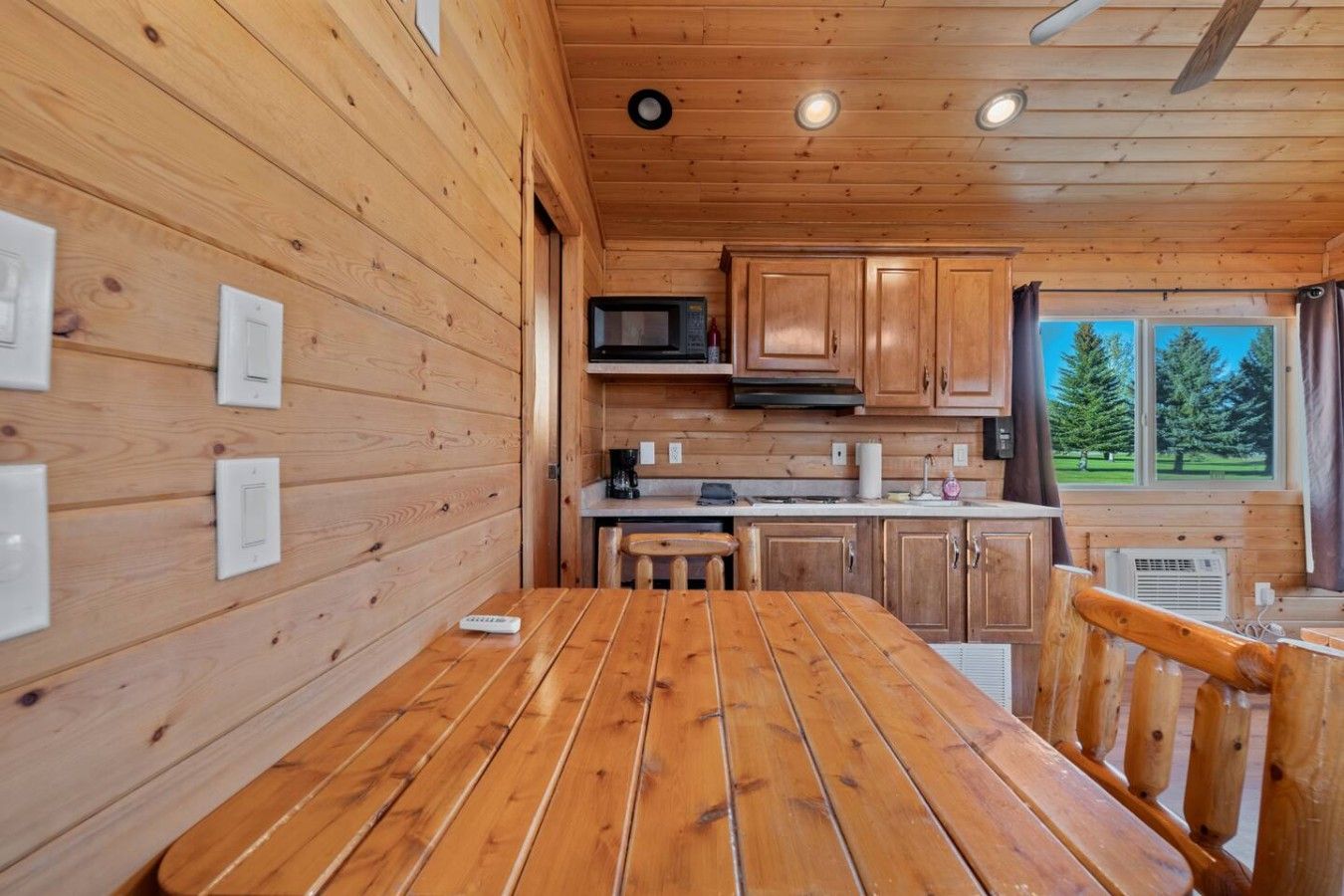 Un intérieur en bois comprenant une table à manger, un coin cuisine et une fenêtre donnant sur la forêt.