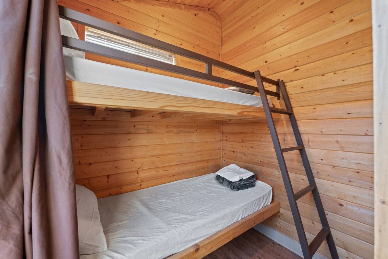 Un lit superposé avec une échelle, des murs en bois et une fenêtre.