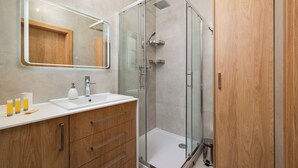 Een moderne badkamer met een douchecabine van glas, een houten wastafelmeubel met een spiegel en een witte wasbak.