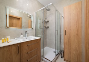 Une salle de bain moderne avec une douche à parois de verre, un meuble-lavabo en bois avec un miroir et un lavabo blanc.