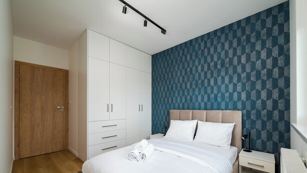 Een slaapkamer met een bed, een kledingkast, een nachtkastje en een muur met een geometrisch patroon.