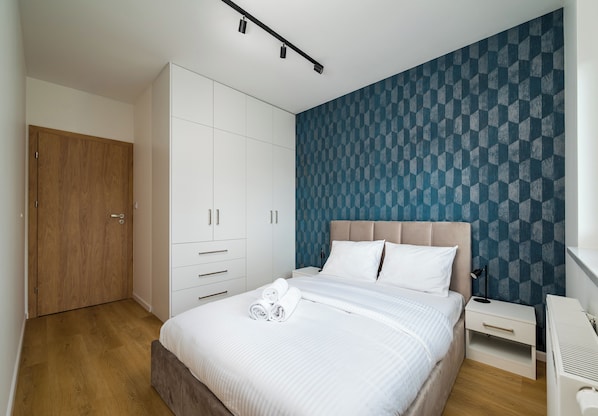 Une chambre à coucher comprenant un lit, une armoire, une table de chevet et un mur orné d’un motif géométrique.