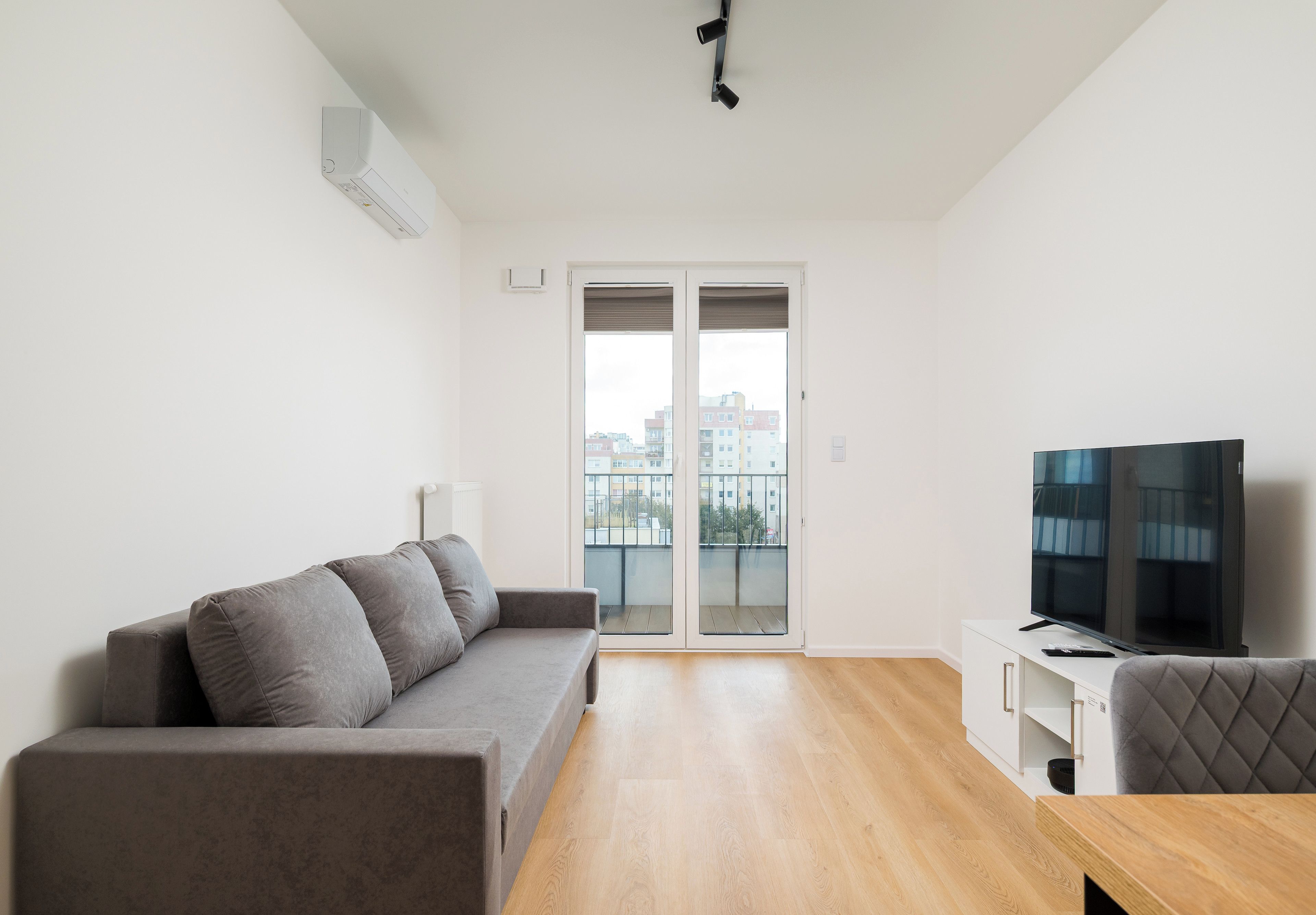 Een moderne woonkamer met een grijze bank, een flatscreen televisie en een houten vloer.