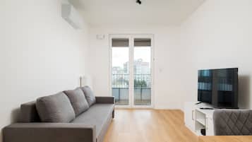 Een moderne woonkamer met een grijze bank, een flatscreen televisie en een houten vloer.