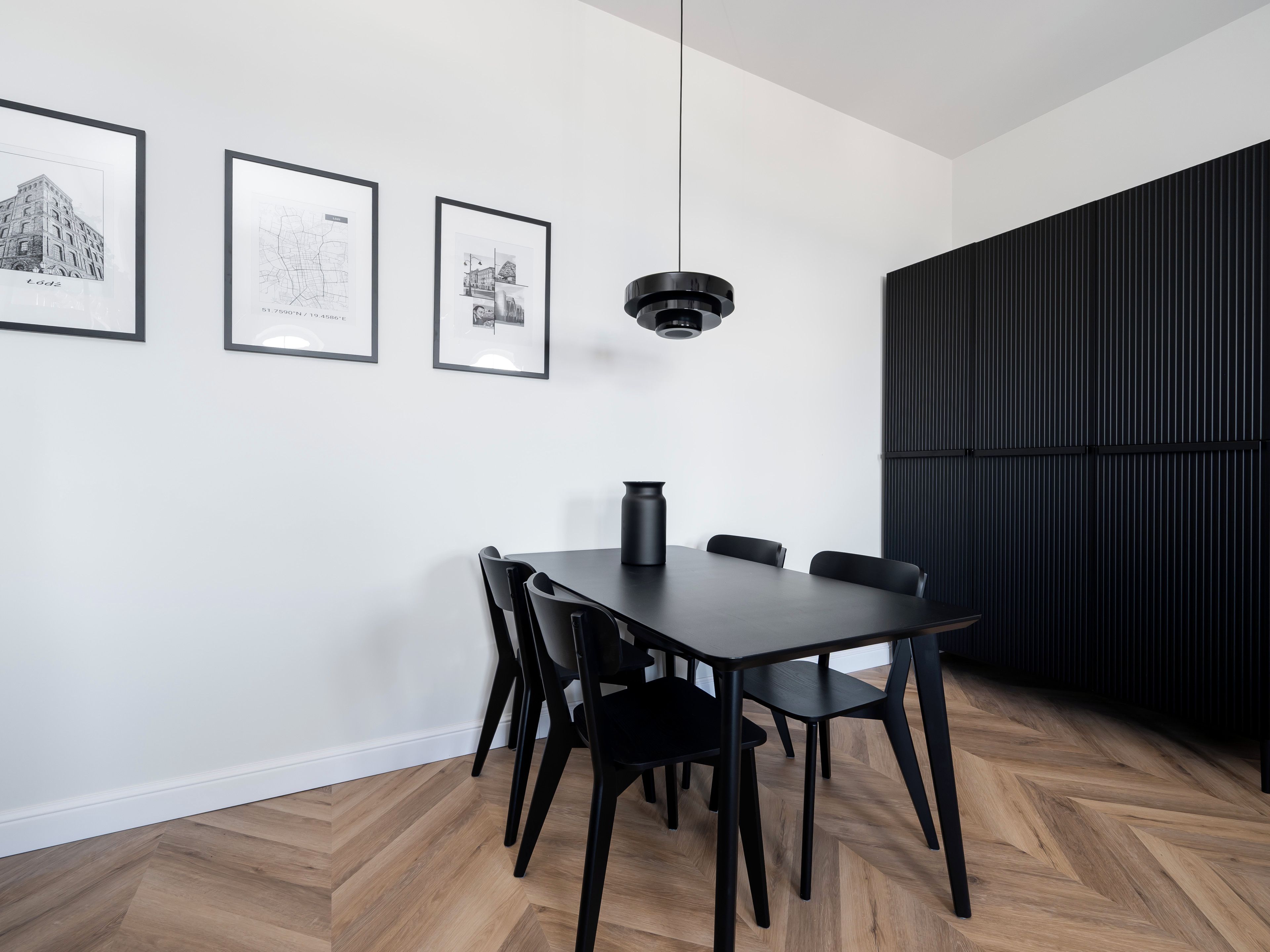 Un espace repas moderne avec une table et des chaises en bois foncé, un luminaire suspendu noir et trois photographies en noir et blanc encadrées accrochées au mur.