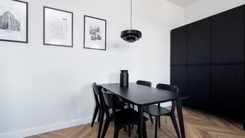 Un espace repas moderne avec une table et des chaises en bois foncé, un luminaire suspendu noir et trois photographies en noir et blanc encadrées accrochées au mur.