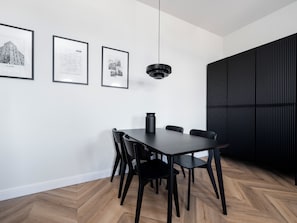 A modern dining area with a dark wooden table and chairs, a black pendant light, and three framed black-and-white photographs on the wall. - Narutowicza 45 Signature Apartment (Łódź)