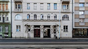 Un immeuble à plusieurs étages, doté d’éléments architecturaux classiques, notamment une entrée centrale avec une porte de couleur sombre et une série de statues au-dessus.