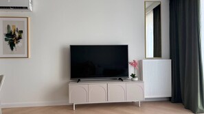 A modern living room with a flat-screen TV on a white cabinet, a radiator, and a mirror on the wall.