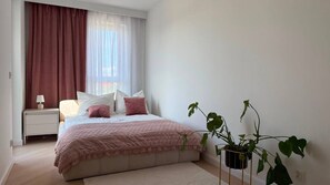 A bedroom with a bed, bedside table, lamp, and potted plants. - Rokietnica Deluxe Apartment (Rokietnica)