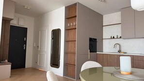 A modern kitchen with built-in appliances, a dining area with a glass table, and a door leading to another room.