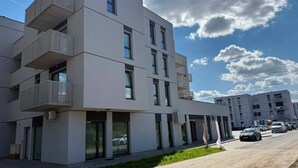 Un immeuble résidentiel moderne à plusieurs étages, doté de balcons, de grandes fenêtres et d’un espace de stationnement avec des voitures.