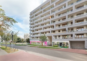 Un immeuble résidentiel à plusieurs étages, doté de balcons, d’un chemin piétonnier et d’une devanture de magasin avec une enseigne.