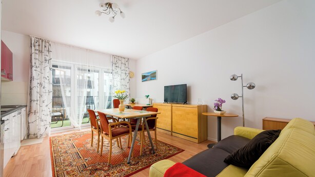 Een woonkamer met een bank, een eettafel met stoelen, een televisie en een keuken met kasten.