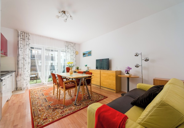Un salon comprenant un canapé, une table à manger avec des chaises, un téléviseur et un coin cuisine avec des placards.