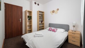 Een slaapkamer met een bed, een nachtkastje, een dressoir, een houten garderobe en twee boekenkasten.