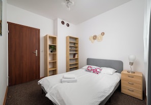 Une chambre à coucher comprenant un lit, une table de chevet, une commode, une armoire en bois et deux étagères.